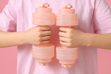 Woman holding dumbbells on pink background, closeupの写真素材