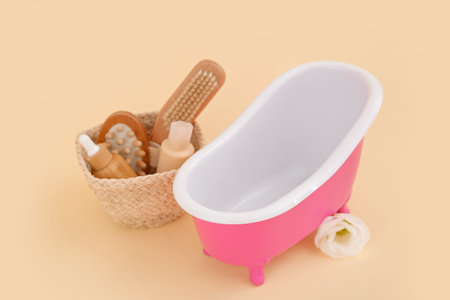 Small bathtub and basket with bath supplies on color background