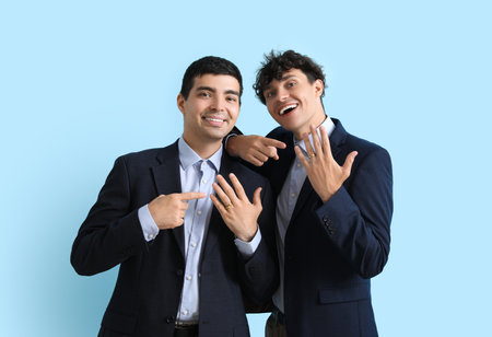 Married gay couple pointing at their wedding rings on blue backgroundの写真素材