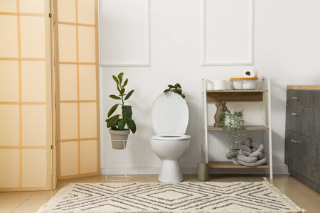 Interior of light restroom with ceramic toilet bowl, shelving unit and houseplantsの写真素材