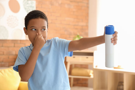 Little African-American boy disgusted by bad smell using air freshener in living room