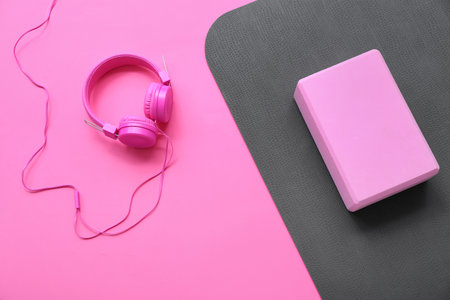Yoga mat with foam exercise block and headphones on pink backgroundの写真素材