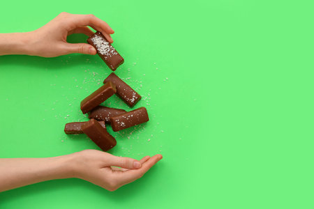 Woman eating tasty chocolate covered coconut candies on green backgroundの写真素材