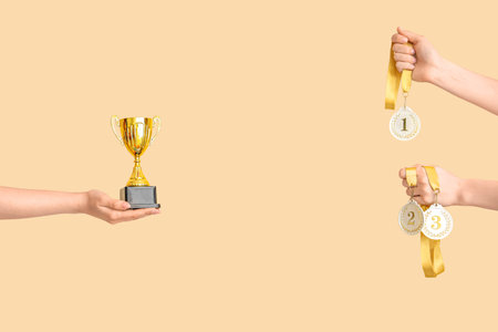 Female hands with gold cup and medals on beige background