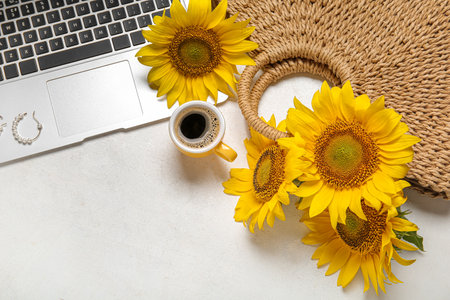 Modern laptop, cup of coffee, sunflowers and rattan bag on light backgroundの写真素材
