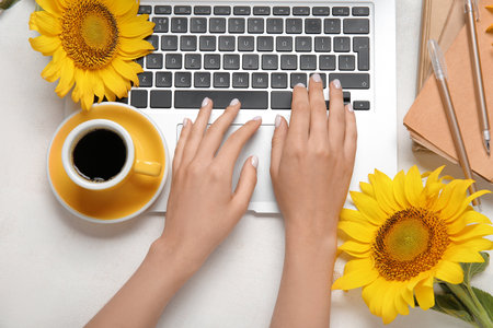 Woman with modern laptop, sunflowers and cup of coffee on light backgroundの写真素材