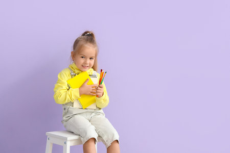 Cute little girl with notebooks, pencils and brushes on lilac backgroundの写真素材