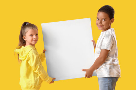 Cute little children with blank poster on yellow backgroundの写真素材