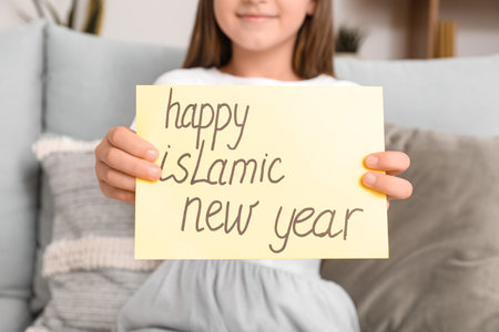 Little Muslim girl with greeting card for Islamic New Year at homeの写真素材