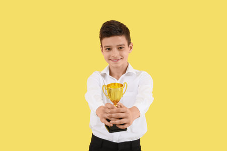 Smart little school boy with prize cup on yellow background