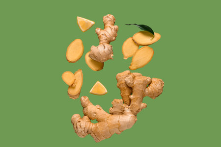 Flying slices of fresh ginger root and lemon on green background
