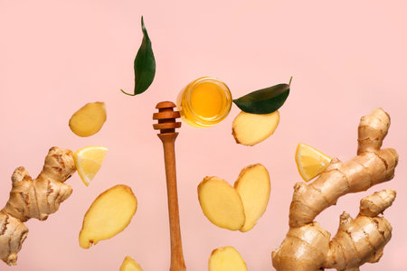 Flying slices of fresh ginger root and jar with honey on pink backgroundの写真素材
