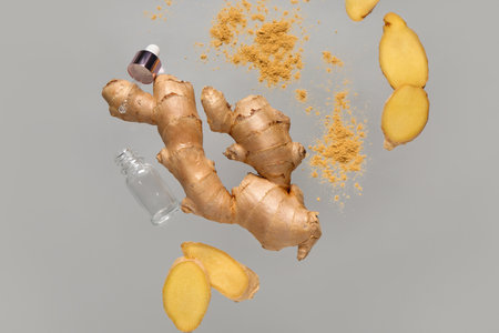 Flying slices of fresh ginger root with dried powder and cosmetic bottle on gray backgroundの写真素材