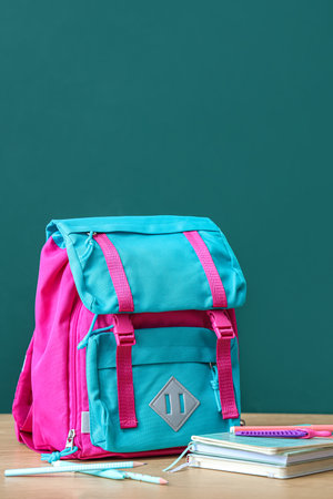 Colorful school backpack with stationery on brown wooden table near green chalkboardの写真素材