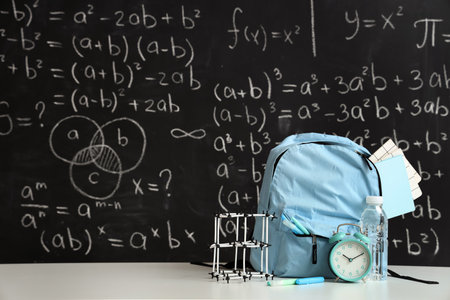 Blue school backpack with stationery, molecular model and bottle of water on white table near black chalkboardの写真素材