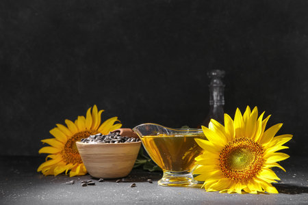 Gravy boat of sunflower oil and wooden bowl with seeds on black backgroundの写真素材