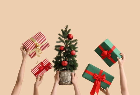 Hands holding Christmas tree and gifts on beige backgroundの写真素材