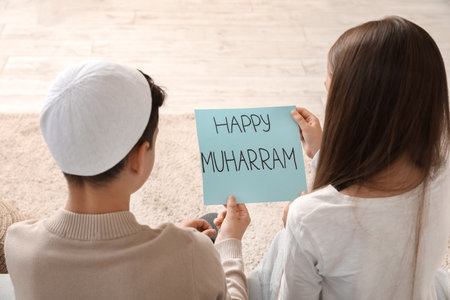 Little Muslim children with greeting card for Islamic New Year at homeの写真素材