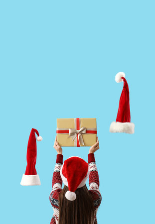 Woman holding Christmas gift and Santa Claus hats on light blue background, back viewの写真素材