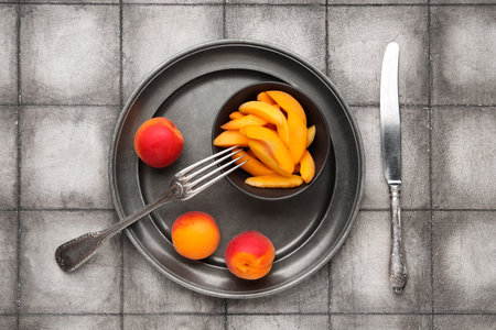 Plate with sweet apricots and bowl of pieces on gray tile backgroundの写真素材