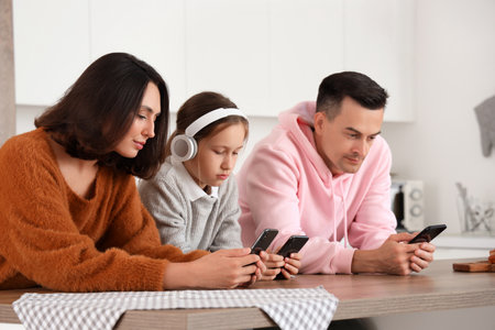 Family involved with mobile phones at table in kitchenの写真素材