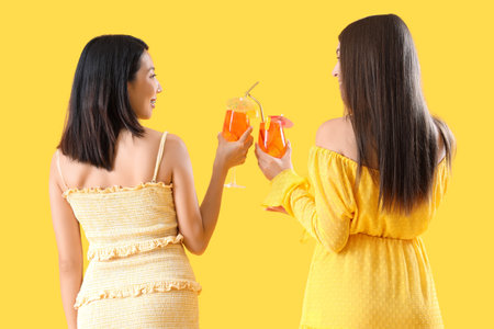 Beautiful young women with glasses of tasty spritz cocktail on yellow background, back viewの写真素材