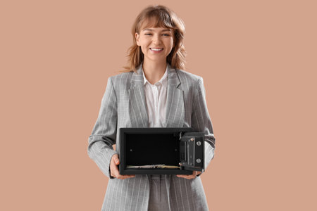 Beautiful young happy woman with safe box and money on brown backgroundの写真素材