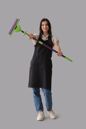 Young woman with floor mop on gray background