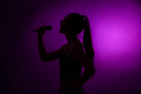 Silhouette of woman with modern microphone singing on dark background
