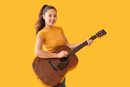 Young woman playing guitar on yellow backgroundの写真素材