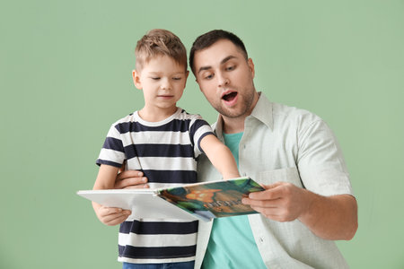 Shocked father and his little son reading book together on green backgroundの写真素材