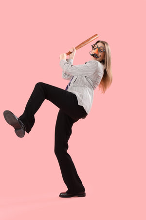 Young businesswoman in funny disguise with baseball bat on pink backgroundの写真素材