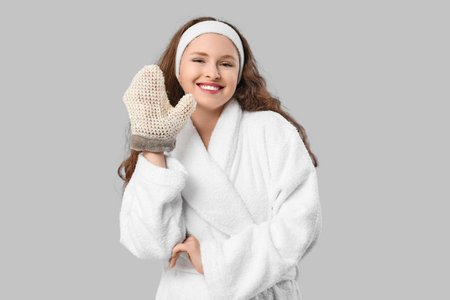Beautiful young happy woman in bathrobe with bath massage mitten on gray backgroundの写真素材