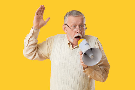 Shocked senior man with megaphone on yellow backgroundの写真素材