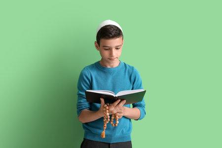 Little Muslim boy with Quran and praying beads on green backgroundの写真素材