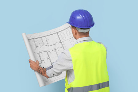 Young male engineer with blueprint on blue background, back view