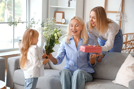 Cute little girl and her mother greeting granny with gifts at home