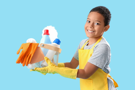 Little African-American boy with cleaning supplies in basket on blue backgroundの写真素材