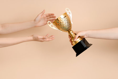 Female hands receiving gold cup on beige backgroundの写真素材