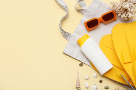 Beach accessories and bottle of sunscreen on beige background