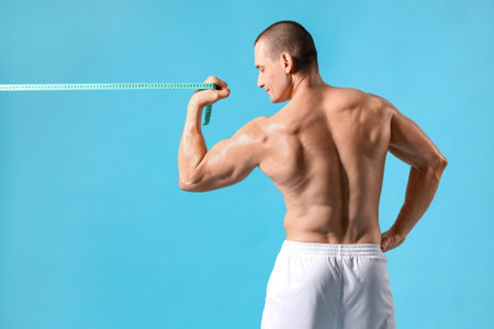 Male bodybuilder with tape measure on blue background, back viewの写真素材