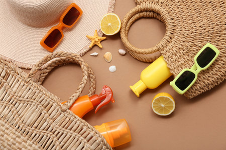 Bottles with sunscreen cream, sunglasses and bags on brown background