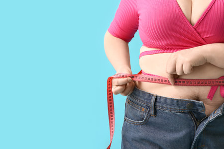 Overweight woman measuring waist on blue background, closeup. Diet conceptの写真素材
