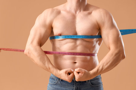 Male bodybuilder with measuring tapes on beige background, closeupの写真素材