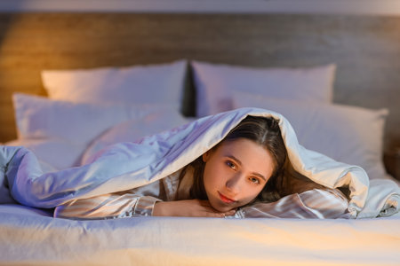 Young woman lying under blanket in bedroom at nightの写真素材