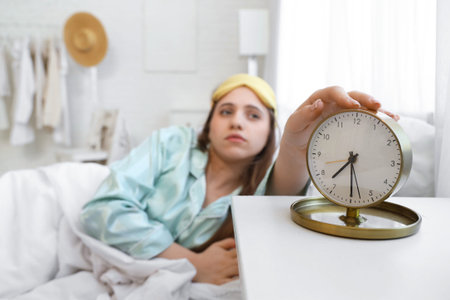 Young woman turning off alarm clock in bedroom, closeup