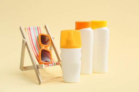 Bottles of sunscreen cream, deckchair and sunglasses on beige backgroundの写真素材