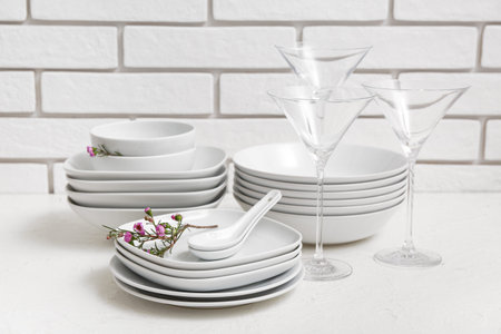 Beautiful tableware with flowers on white table near brick wallの写真素材