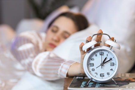 Young woman turning off alarm clock in bedroom, closeup