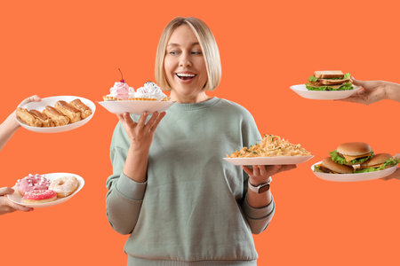Beautiful woman and hands with unhealthy food on orange background. Overeating conceptの写真素材